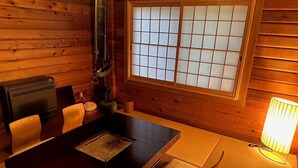 A wooden interior with a tatami mat table, a traditional Japanese room divider, a shoji screen window, and a heater.