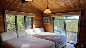 A wooden cabin bedroom with two beds, large windows, and a painting on the wall.
