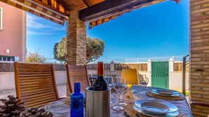 An outdoor dining area with a table set for two, featuring a bottle of wine, glasses, and a water bottle.