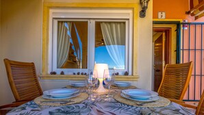 A dining table set for four with a tropical leaf pattern tablecloth, two wooden chairs, and a window with curtains.
