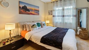 A bedroom with a bed, bedside lamps, a painting, a mirror, and a window with curtains.