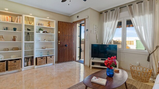 A living room with a TV, a ceiling fan, a bookshelf, and a window with curtains.