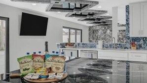 Una cucina moderna con un piano di lavoro in marmo, un soffitto nero e una parete divisoria con motivo blu e bianco. Sul piano ci sono diversi alimenti, tra cui sacchetti di chips Miss Vickie's.