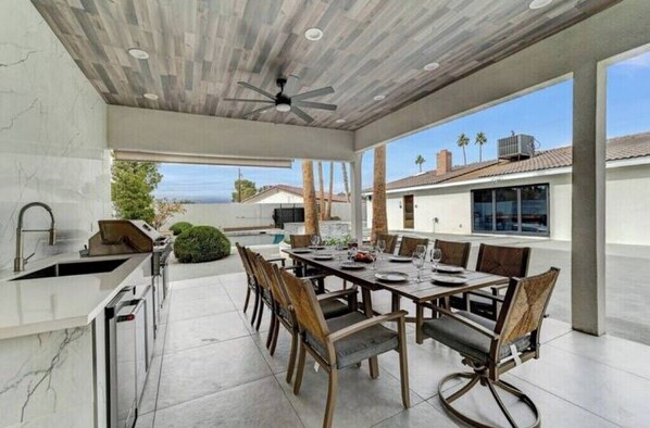 A spacious outdoor dining area with a modern kitchen, large windows, and a view of the landscape.