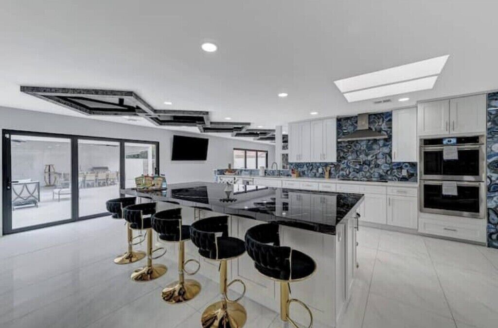 A modern kitchen with a central island, bar stools, and a large window.