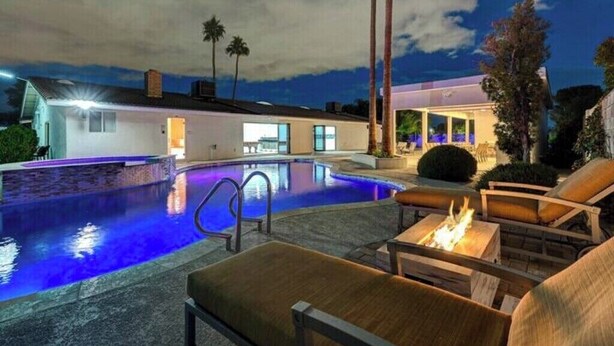 Una piscina con un braciere e sedie a sdraio, circondata da palme e una casa moderna.