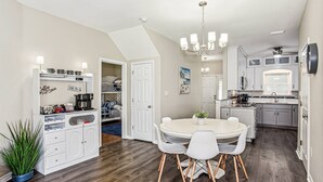 A modern kitchen with a dining area, featuring a white cabinet with coffee mugs, a chandelier, and a dining table with chairs. - Majestic Retreat - Navarre Townhouse With Bay Access, Garage Community Pool, Kayak, and Paddleboard (Navarre)