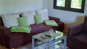 En stue med træloft, sofaarrangement, sofabord i glas og et billede af en skov.