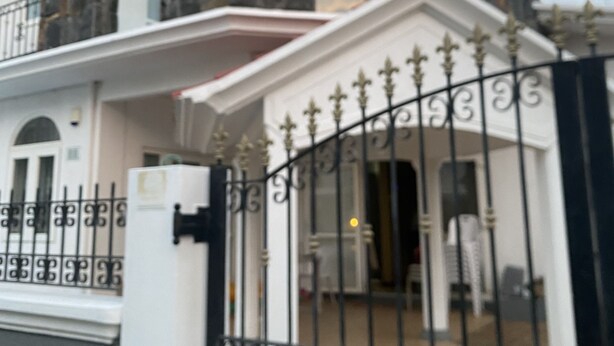 A two-story house with a gated entrance, a balcony, and a stone facade.