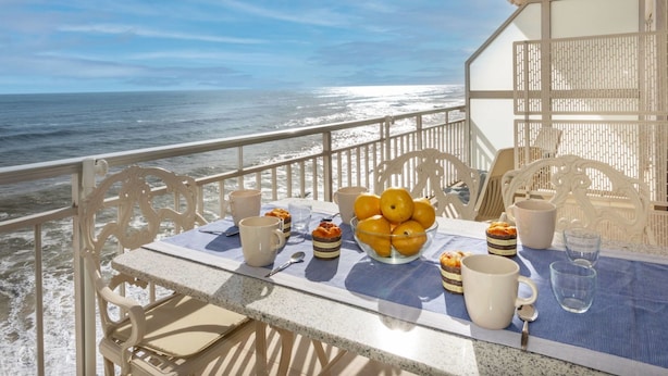 A table set with a bowl of lemons, a cup, and a glass on a balcony overlooking the ocean.