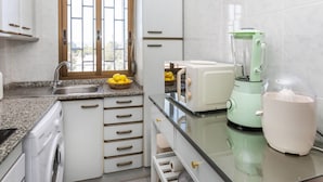 A modern kitchen with a granite countertop, a built-in dishwasher, a window with a view, and a green blender.