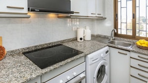 A modern kitchen with white cabinets, a black range hood, a built-in oven, a washing machine, and a granite countertop.
