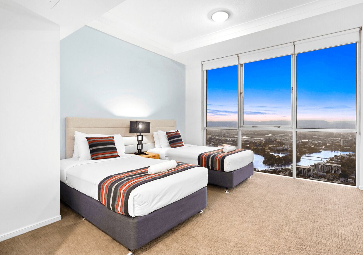 A hotel room with two beds, a large window with a city view, and a carpeted floor.
