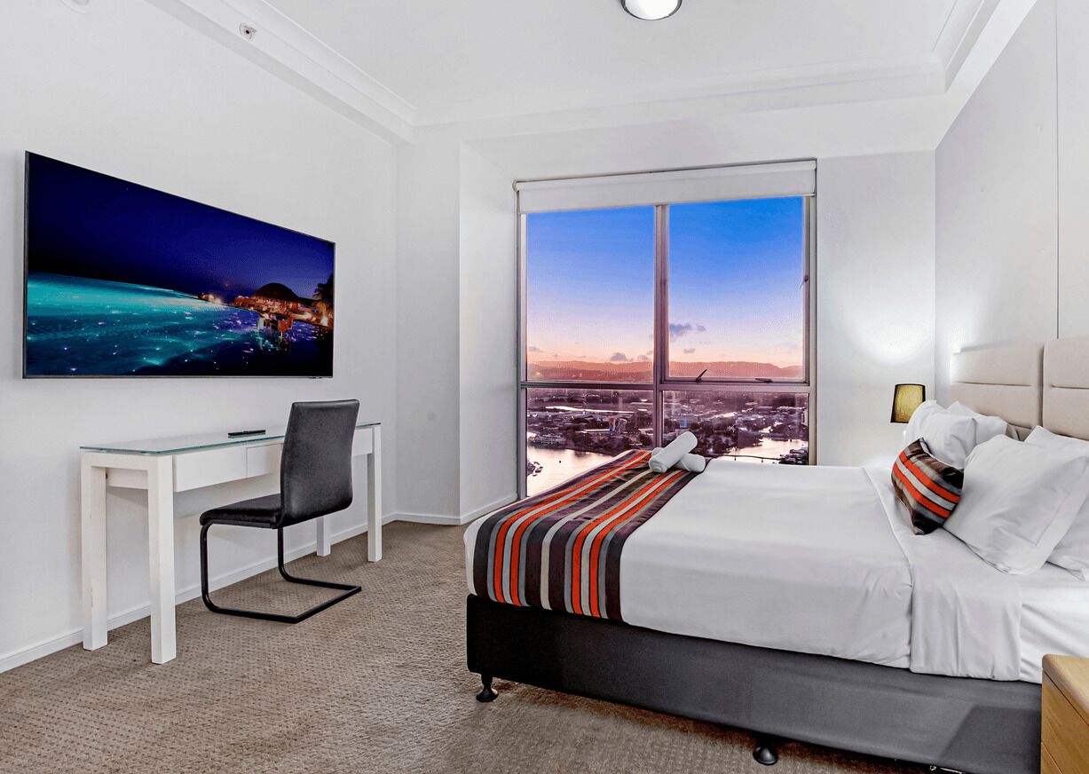 Una camera d'albergo con un letto, una scrivania e un'ampia finestra vista città.