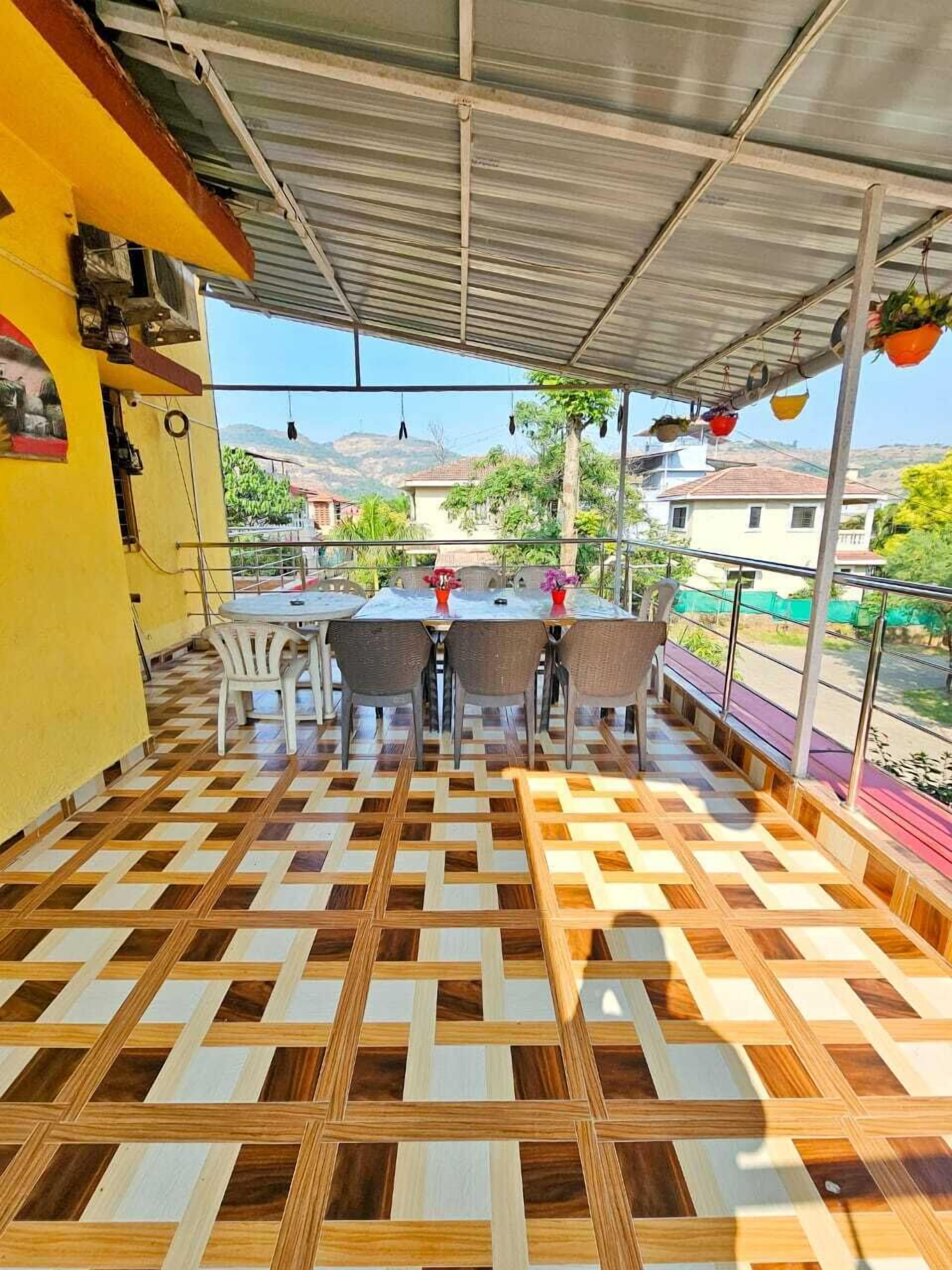 Un patio couvert avec un sol à carreaux, une table entourée de chaises et des plantes suspendues.