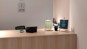 A reception desk with a clock, a sign indicating the reception area, and a digital display board. - Private room 8m for men. Bed, AC, side table, Wi-Fi. Shared baths, lounges. (Buraydah)