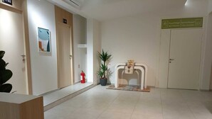 A clean, modern lobby with a reception desk, a fire extinguisher, a potted plant, and a sign indicating the location of the bathroom and lounge. - Private room 8m for men. Bed, AC, side table, Wi-Fi. Shared baths, lounges. (Buraydah)