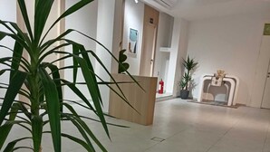 A reception area with a reception desk, a potted plant, a fire extinguisher, and a fireplace. - Private room 8m for men. Bed, AC, side table, Wi-Fi. Shared baths, lounges. (Buraydah)
