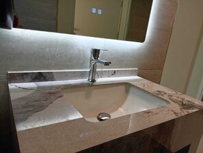 Un lavamanos de diseño moderno, un espejo encima y una pared con azulejos.