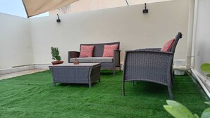 A patio with artificial grass, wicker furniture, and a potted plant. - Private room 8m for men. Bed, AC, side table, Wi-Fi. Shared baths, lounges. (Buraydah)