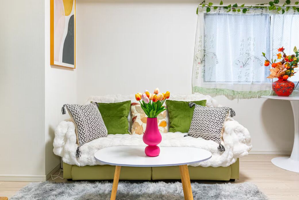 A living room with a green sofa, a white round table, and a pink vase with flowers.