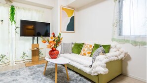 A living room with a sofa, a TV, a small table with a vase of flowers, and a window with curtains. - New Ueno Station 7 Min Walk Inarimachi (Tokyo)