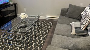 Ein Wohnzimmer mit einem Glastisch, einem grauen Sofa und einem Teppich mit Muster.