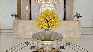 A reception area with a marble reception desk, a glass-top table, and a yellow flower arrangement. - SEDONA Hotel Viet Yen (Viet Yen)