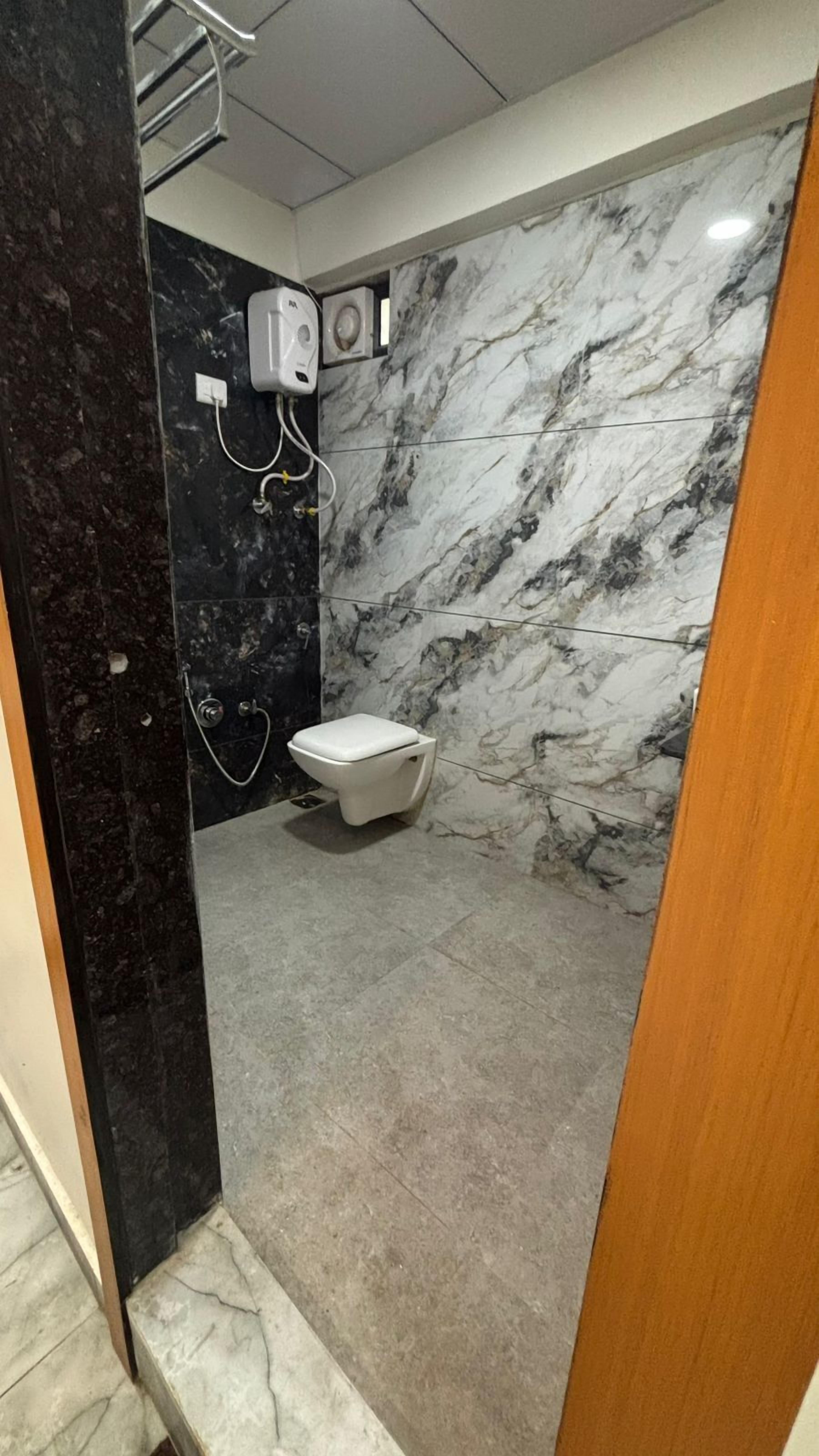 Ein modernes Badezimmer mit Marmorwand, Toilette und Duschbereich.