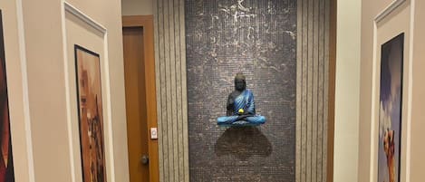 A hallway with a Buddha statue, framed artwork, and a marble floor.