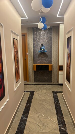 A hallway with a Buddha statue, framed artwork, and a marble floor. - HOTEL BLUE SKY (Ahmedabad)