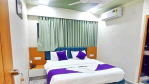 Habitación de hotel con cama, mesita de noche, ventilador de techo y aire acondicionado.