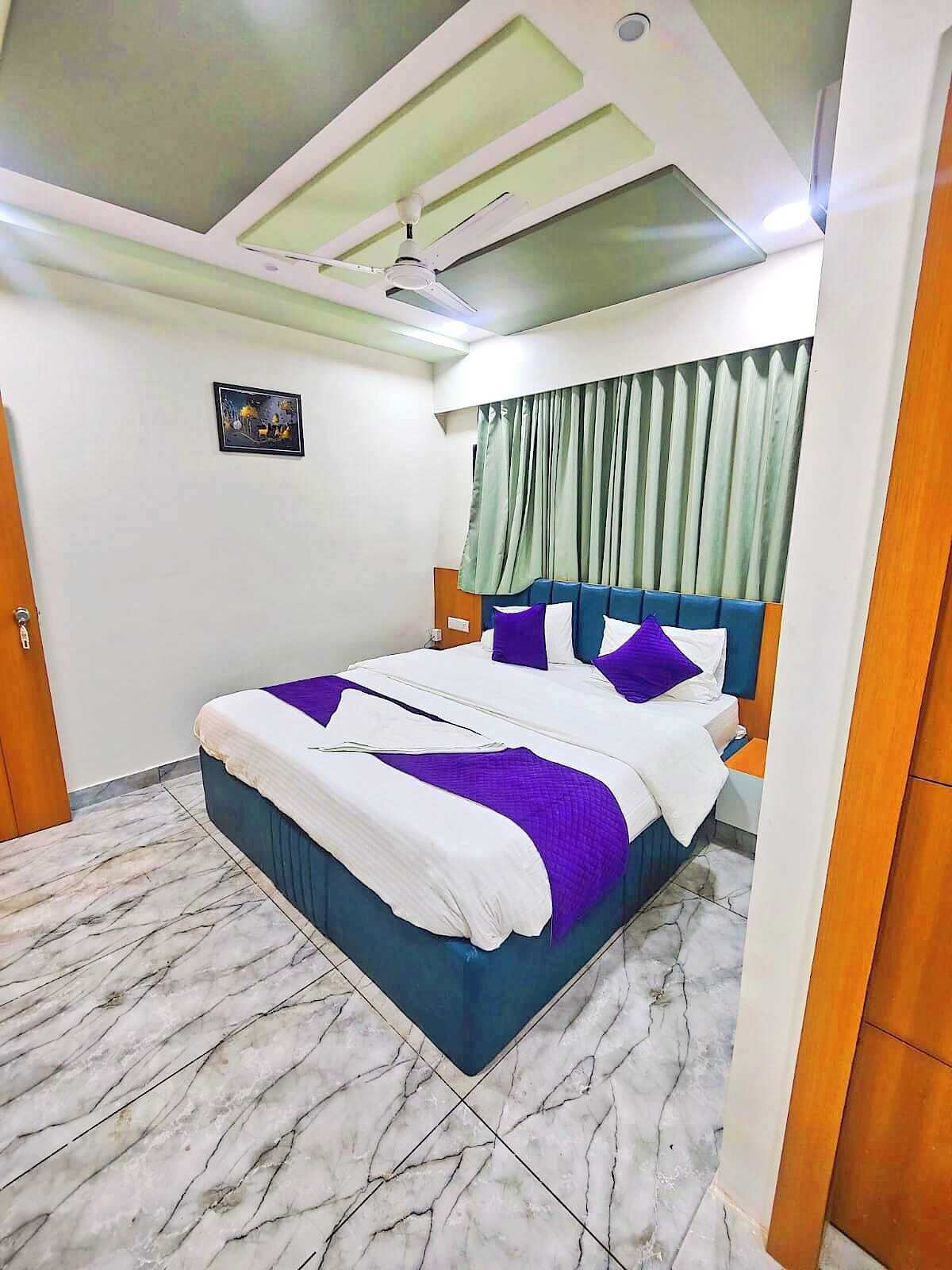 A hotel room with a bed, a ceiling fan, a window with curtains, and a marble floor.