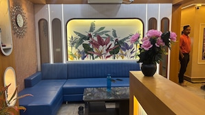 Un interior moderno con una zona de estar tapizada en azul, una mesa con superficie de vidrio y un ventanal con un mural de plantas tropicales.