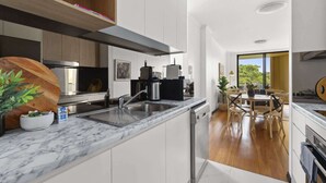 A modern kitchen with marble countertops, stainless steel appliances, and a wooden dining area with a view.
