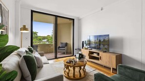 A modern living room with a sofa, a coffee table, a TV, and a sliding glass door leading to an outdoor balcony.