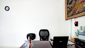 A room with a desk, a laptop, a chair, a clock, and a painting on the wall. - Hotel O Tegalsari Near Tunjungan Plaza (Surabaya)