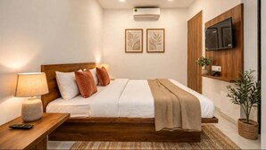 A modern hotel room with a bed, bedside table, lamp, air conditioning unit, wall-mounted TV, and framed artwork. - Hotel Apple (Indore)