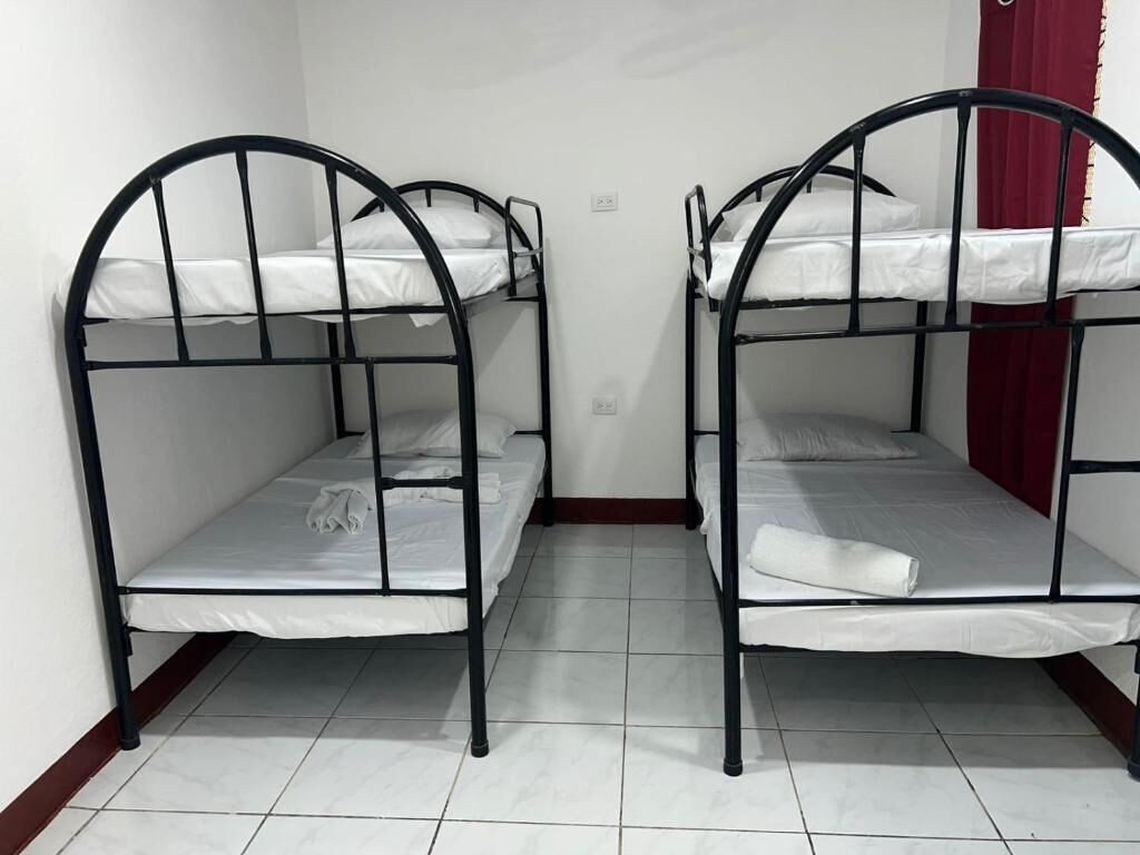 Two bunk beds with white bedding and black metal frames in a room with white tiled flooring and a red curtain.