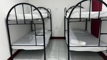 Two bunk beds with white bedding and black metal frames in a room with white tiled flooring and a red curtain.