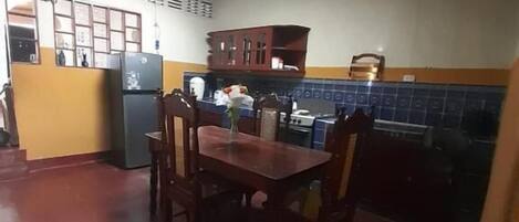 A compact kitchen with a dining table, chairs, a refrigerator, and a tiled backsplash.