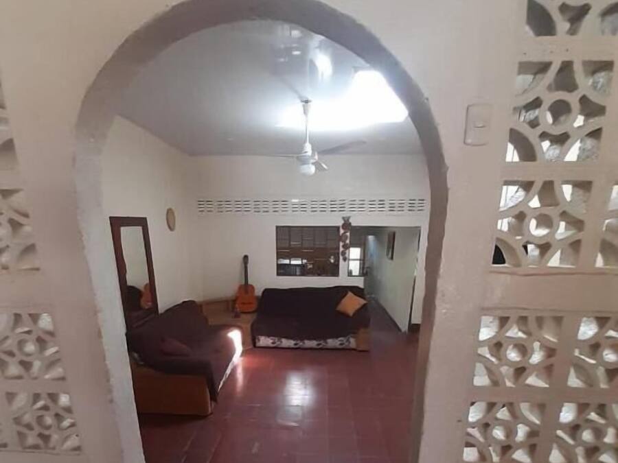 Un espacio interior con suelo de baldosas oscuras, un sofá, una guitarra y un ventilador de techo.