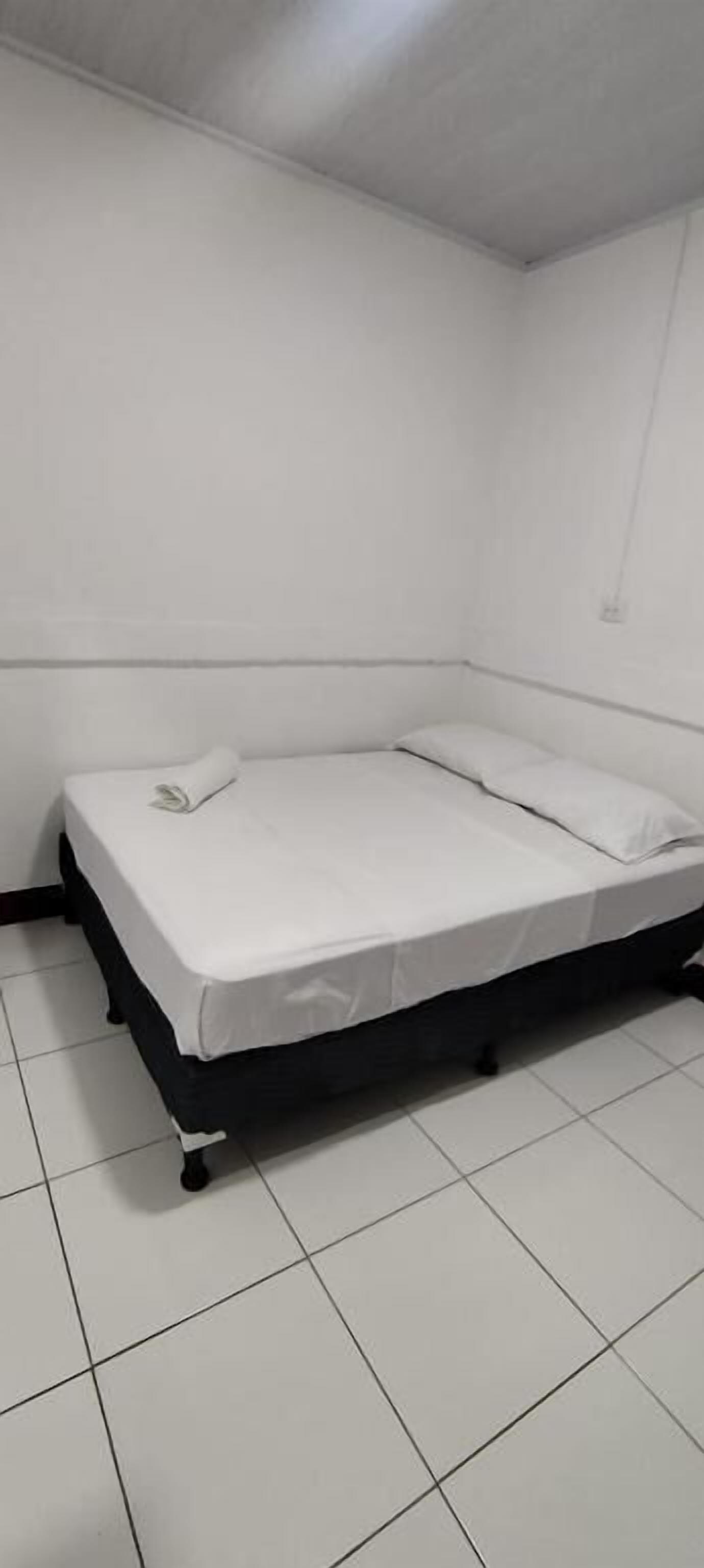 Una habitación pequeña y limpia con una cama individual, paredes blancas y piso de baldosas.