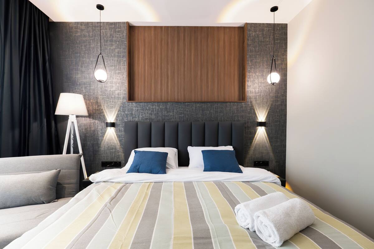 Une chambre d’hôtel moderne avec un grand lit, deux tables de chevet, une lampe et un mur décoratif en bois.