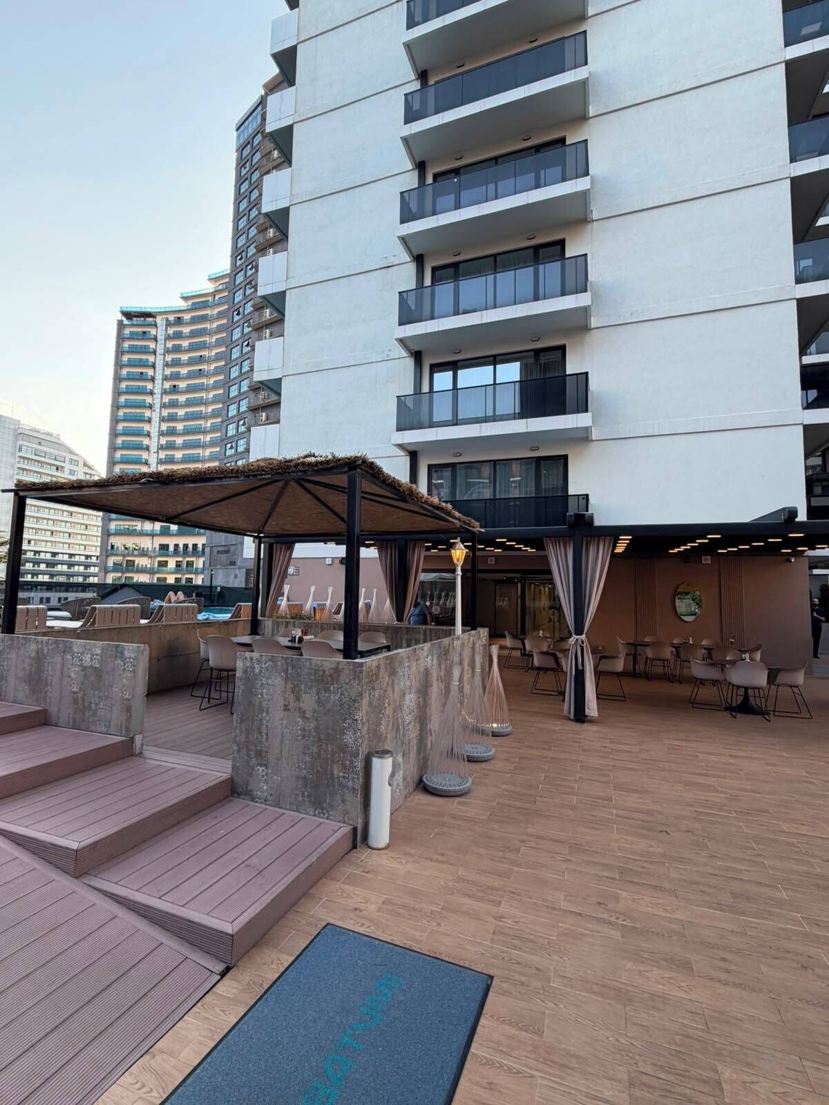 A rooftop terrace with outdoor seating, a pergola, and a view of a high-rise building.