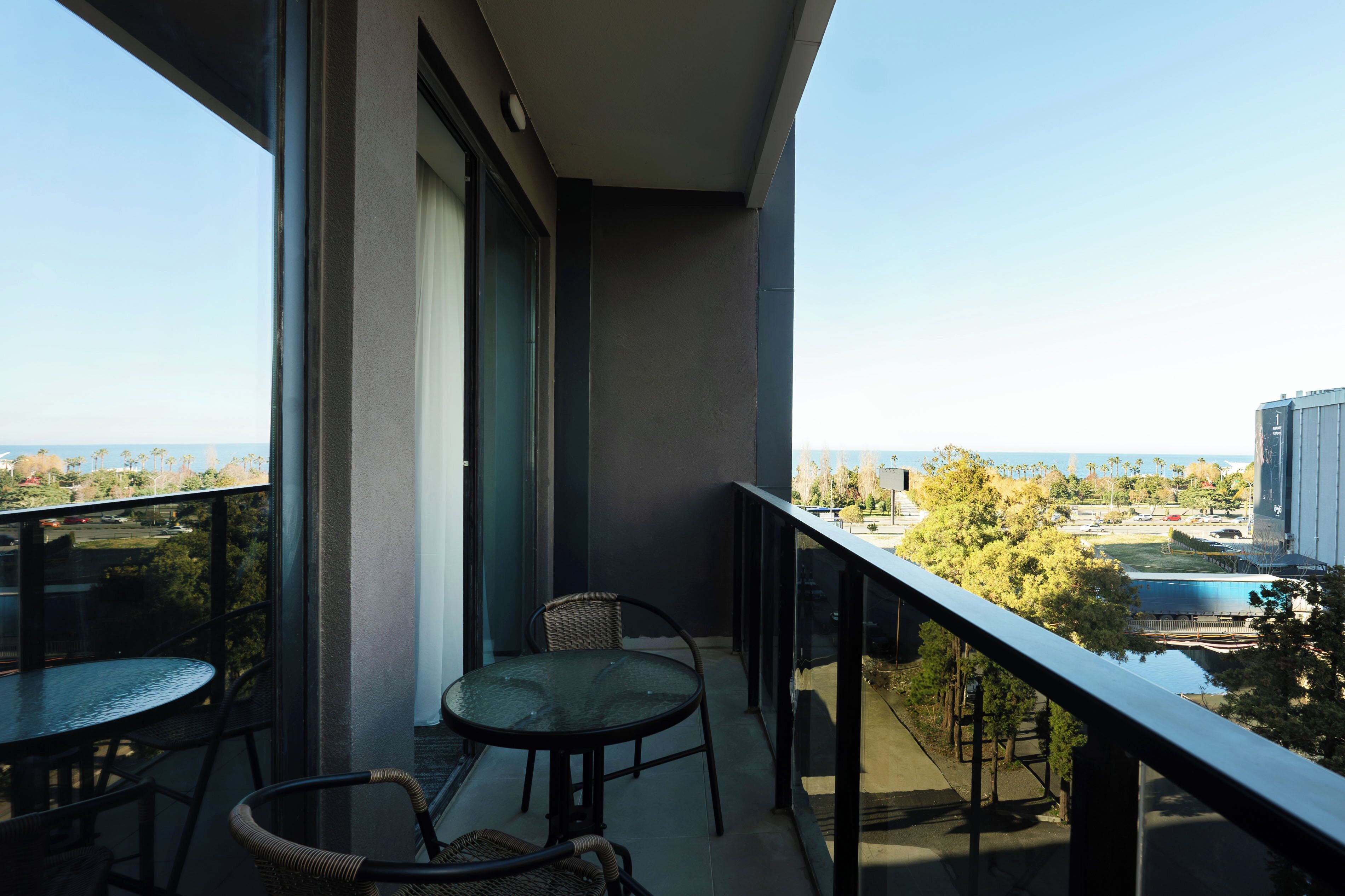 A balcony with a glass table and chairs, offering a view of a pool and surrounding greenery.