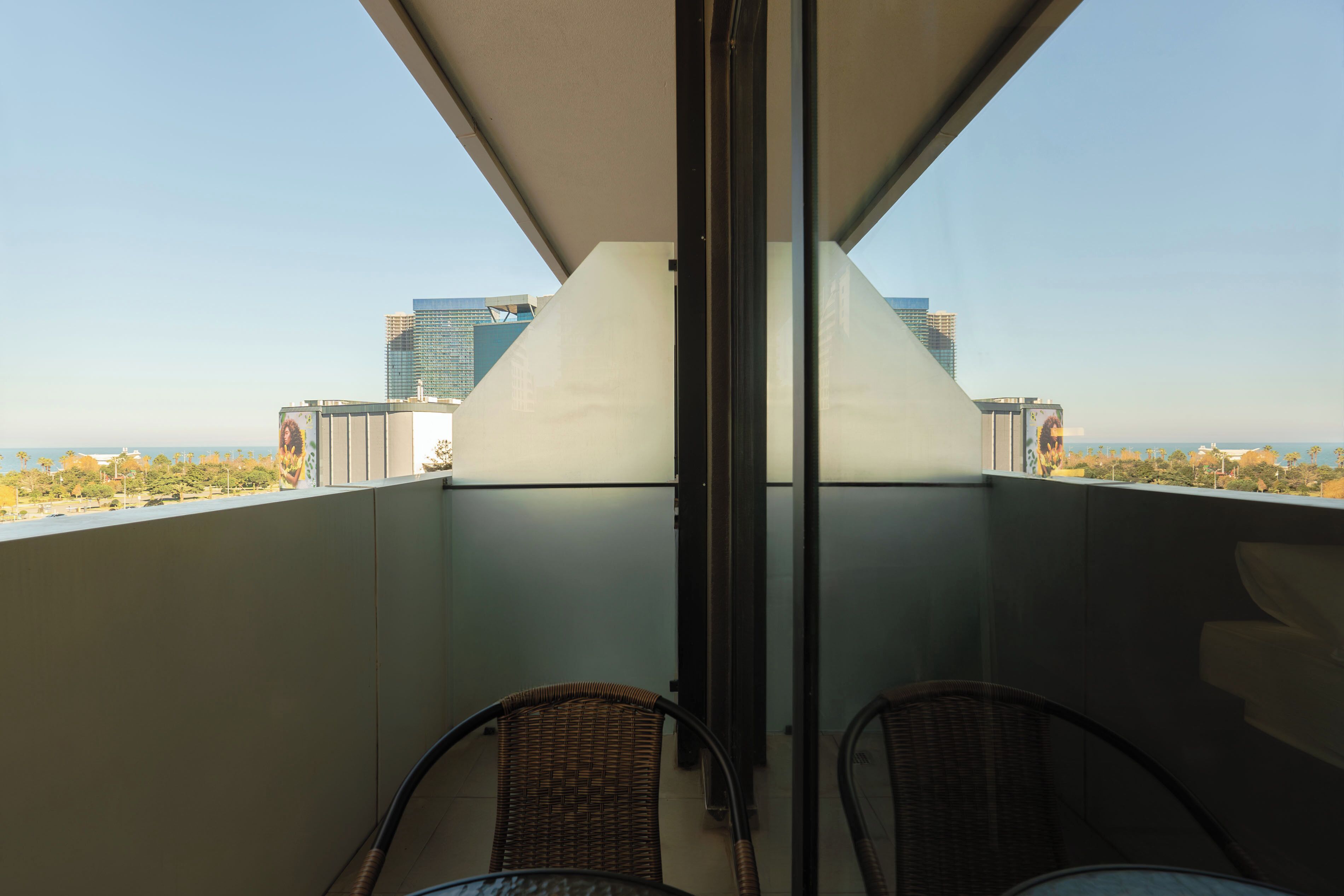 Ein Balkon mit zwei Korbstühlen, einer Glastür und Blick auf Stadt und Meer.