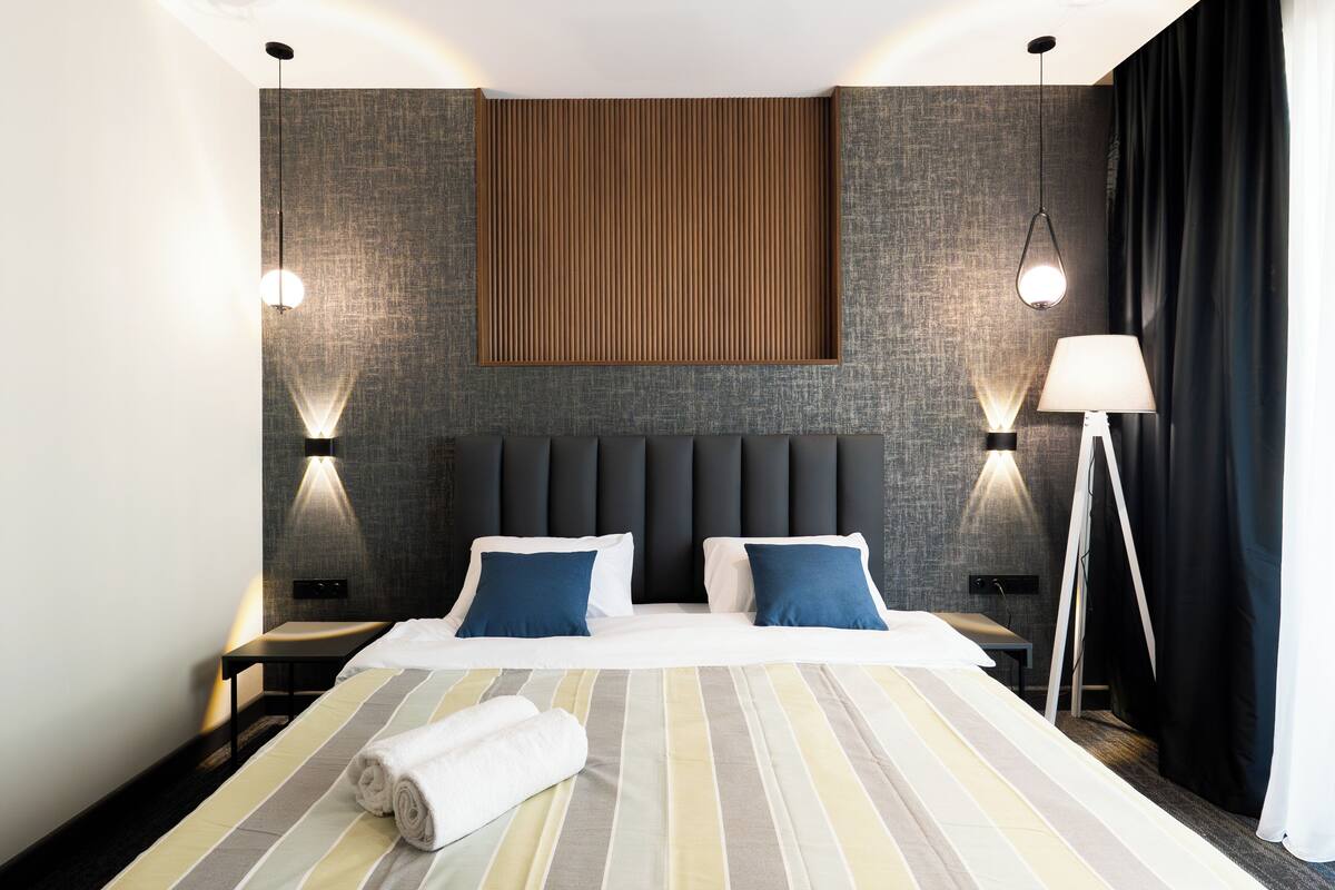 Une chambre d’hôtel moderne avec un grand lit, deux tables de chevet, un panneau lumineux fixé au mur et une lampe sur pied.