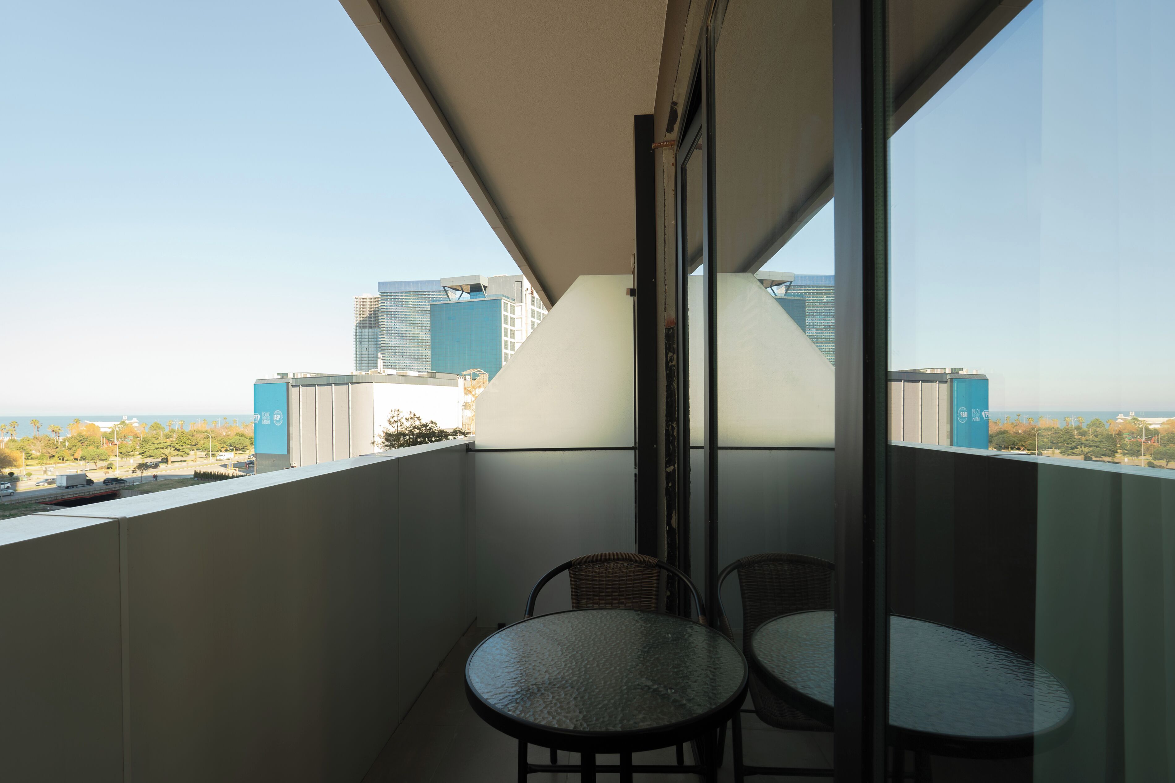 A balcony with two round tables and chairs, a clear view of the cityscape, and a glass door leading to the interior.