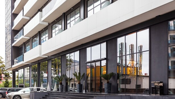 Un edificio moderno con amplios ventanales, una escalera que conduce a la entrada y varias plantas en macetas.